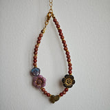 Vibrant pink Czech glass beads are highlighted by blue, purple, and black flower charms and green leaf accents, creating a stunningly attractive design.