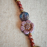 Vibrant pink Czech glass beads are highlighted by blue, purple, and black flower charms and green leaf accents, creating a stunningly attractive design.
