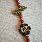 Vibrant pink Czech glass beads are highlighted by blue, purple, and black flower charms and green leaf accents, creating a stunningly attractive design.