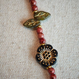 Vibrant pink Czech glass beads are highlighted by blue, purple, and black flower charms and green leaf accents, creating a stunningly attractive design.