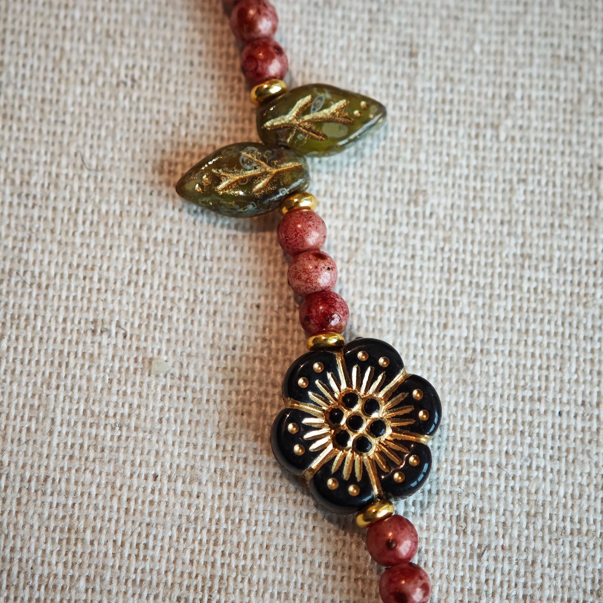 Vibrant pink Czech glass beads are highlighted by blue, purple, and black flower charms and green leaf accents, creating a stunningly attractive design.