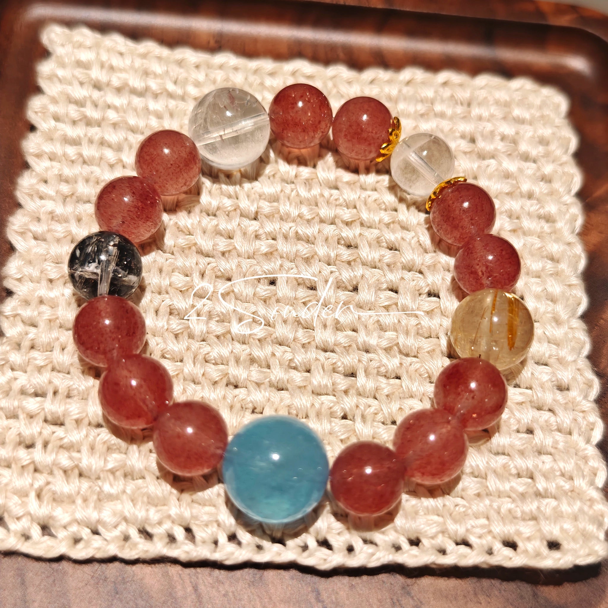 This bracelet is centered around a prominent round light blue aquamarine bead, surrounded by rich reddish-brown strawberry quartz beads. It is accented with clear crystal, black rutilated quartz, and golden rutilated quartz beads, along with delicate gold spacers, creating a harmonious natural stone design.
