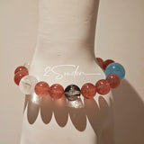 This bracelet is centered around a prominent round light blue aquamarine bead, surrounded by rich reddish-brown strawberry quartz beads. It is accented with clear crystal, black rutilated quartz, and golden rutilated quartz beads, along with delicate gold spacers, creating a harmonious natural stone design.