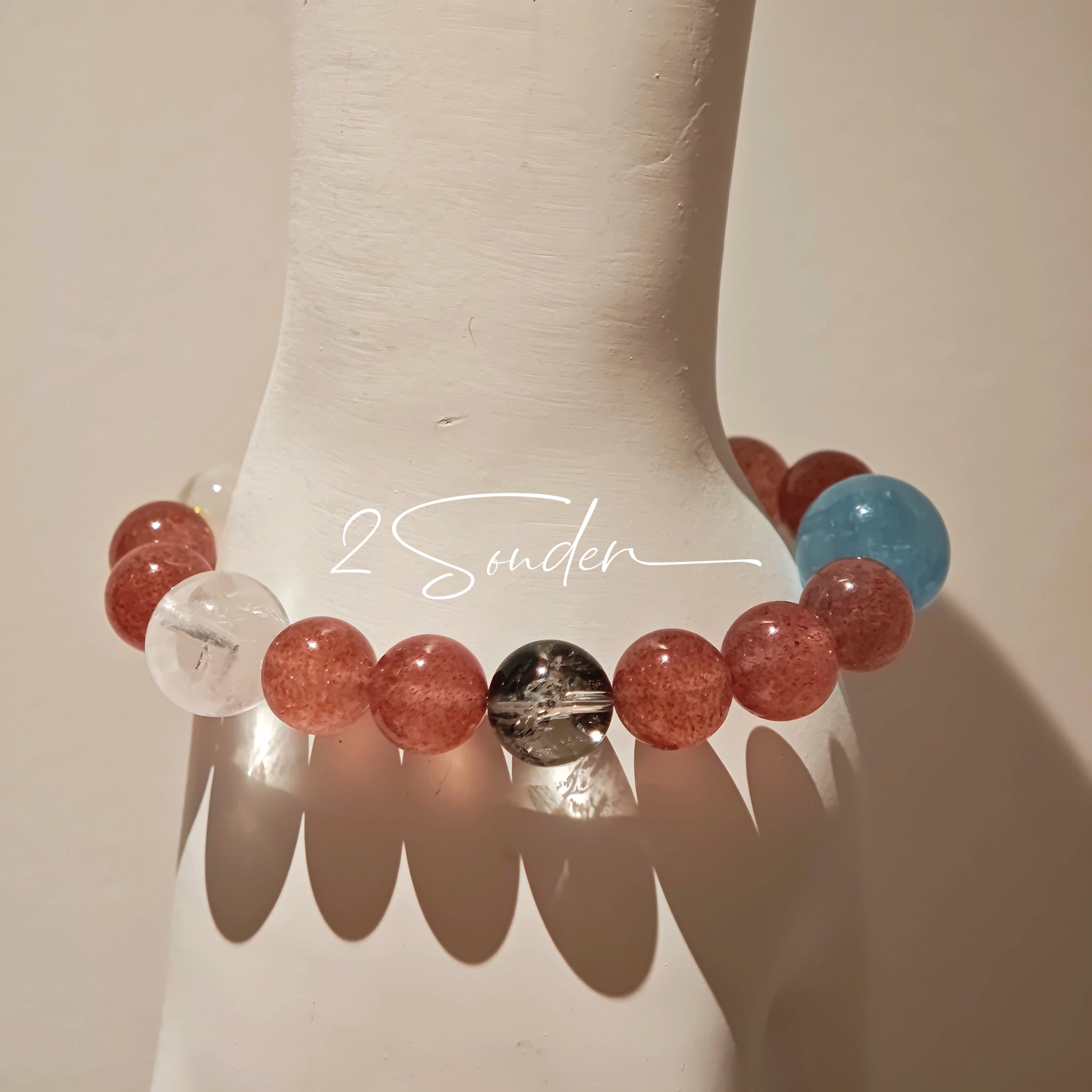 This bracelet is centered around a prominent round light blue aquamarine bead, surrounded by rich reddish-brown strawberry quartz beads. It is accented with clear crystal, black rutilated quartz, and golden rutilated quartz beads, along with delicate gold spacers, creating a harmonious natural stone design.