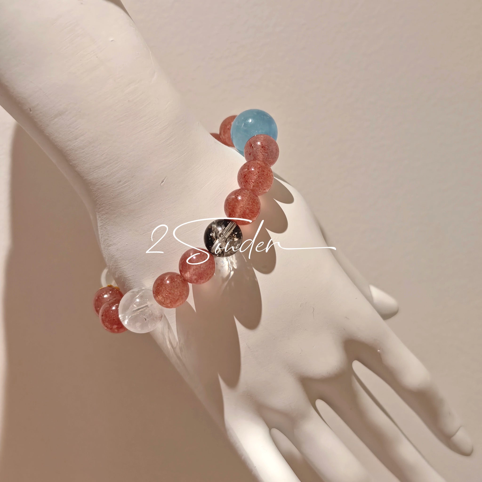 This bracelet is centered around a prominent round light blue aquamarine bead, surrounded by rich reddish-brown strawberry quartz beads. It is accented with clear crystal, black rutilated quartz, and golden rutilated quartz beads, along with delicate gold spacers, creating a harmonious natural stone design.