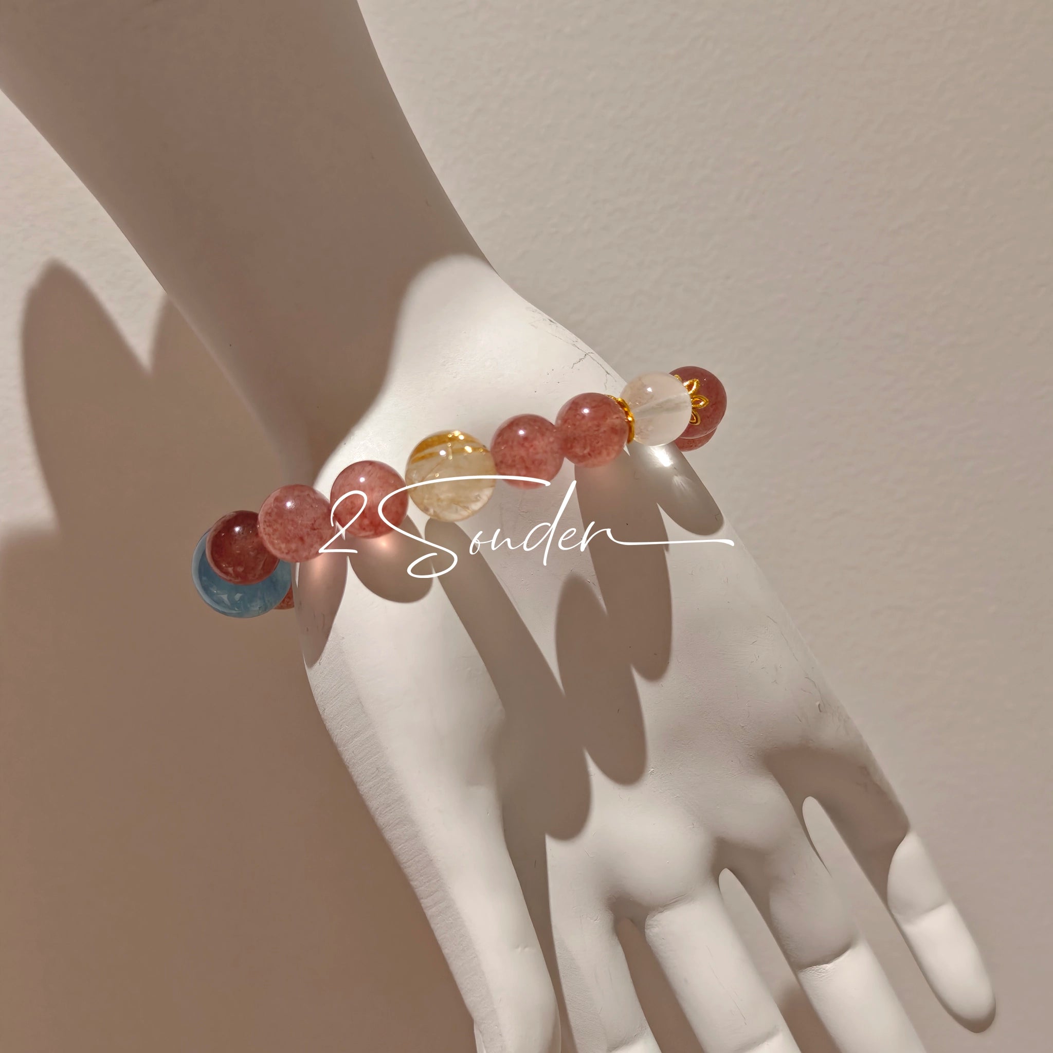 This bracelet is centered around a prominent round light blue aquamarine bead, surrounded by rich reddish-brown strawberry quartz beads. It is accented with clear crystal, black rutilated quartz, and golden rutilated quartz beads, along with delicate gold spacers, creating a harmonious natural stone design.