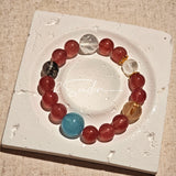 This bracelet is centered around a prominent round light blue aquamarine bead, surrounded by rich reddish-brown strawberry quartz beads. It is accented with clear crystal, black rutilated quartz, and golden rutilated quartz beads, along with delicate gold spacers, creating a harmonious natural stone design.