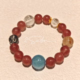 This bracelet is centered around a prominent round light blue aquamarine bead, surrounded by rich reddish-brown strawberry quartz beads. It is accented with clear crystal, black rutilated quartz, and golden rutilated quartz beads, along with delicate gold spacers, creating a harmonious natural stone design.
