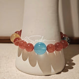 This bracelet is centered around a prominent round light blue aquamarine bead, surrounded by rich reddish-brown strawberry quartz beads. It is accented with clear crystal, black rutilated quartz, and golden rutilated quartz beads, along with delicate gold spacers, creating a harmonious natural stone design.
