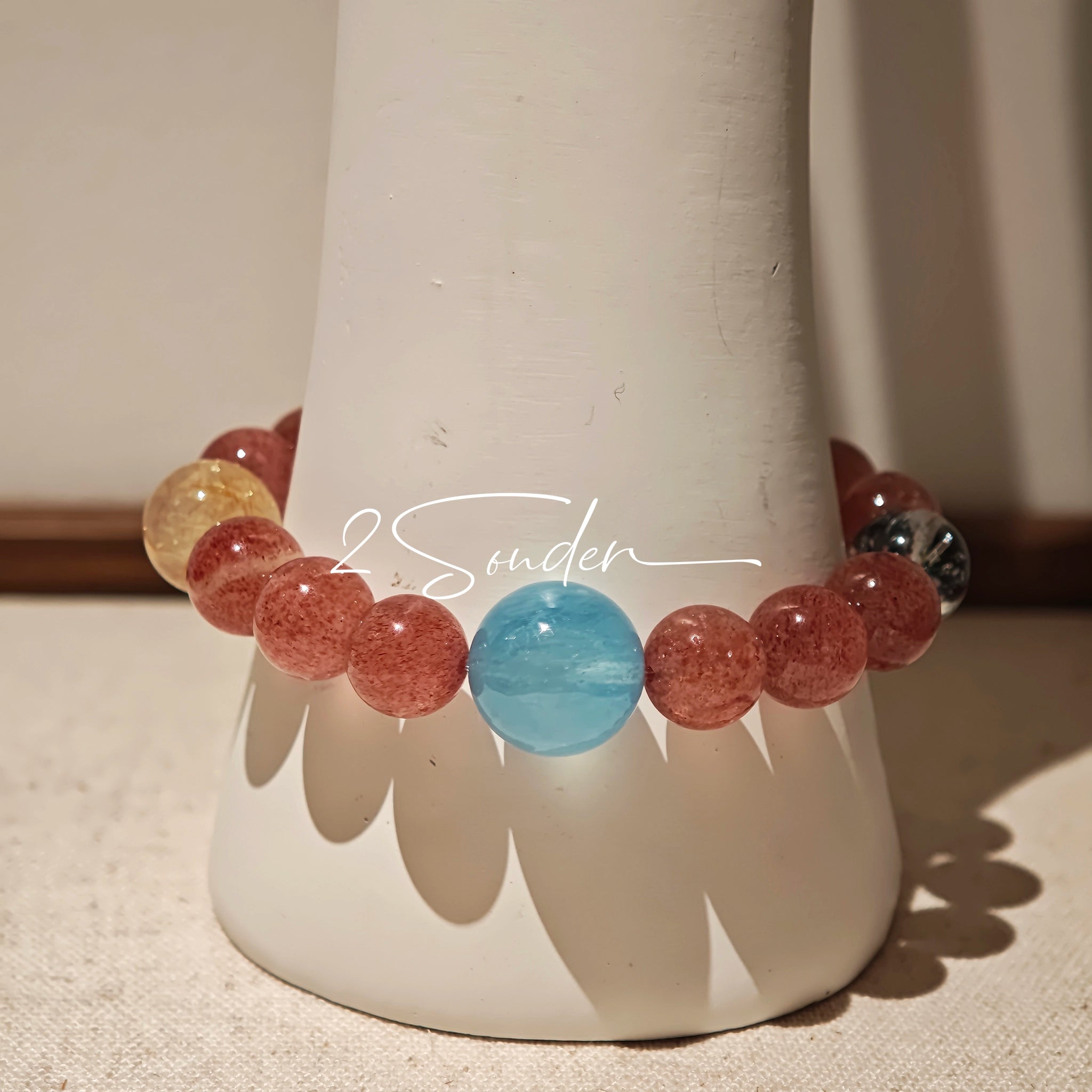 This bracelet is centered around a prominent round light blue aquamarine bead, surrounded by rich reddish-brown strawberry quartz beads. It is accented with clear crystal, black rutilated quartz, and golden rutilated quartz beads, along with delicate gold spacers, creating a harmonious natural stone design.