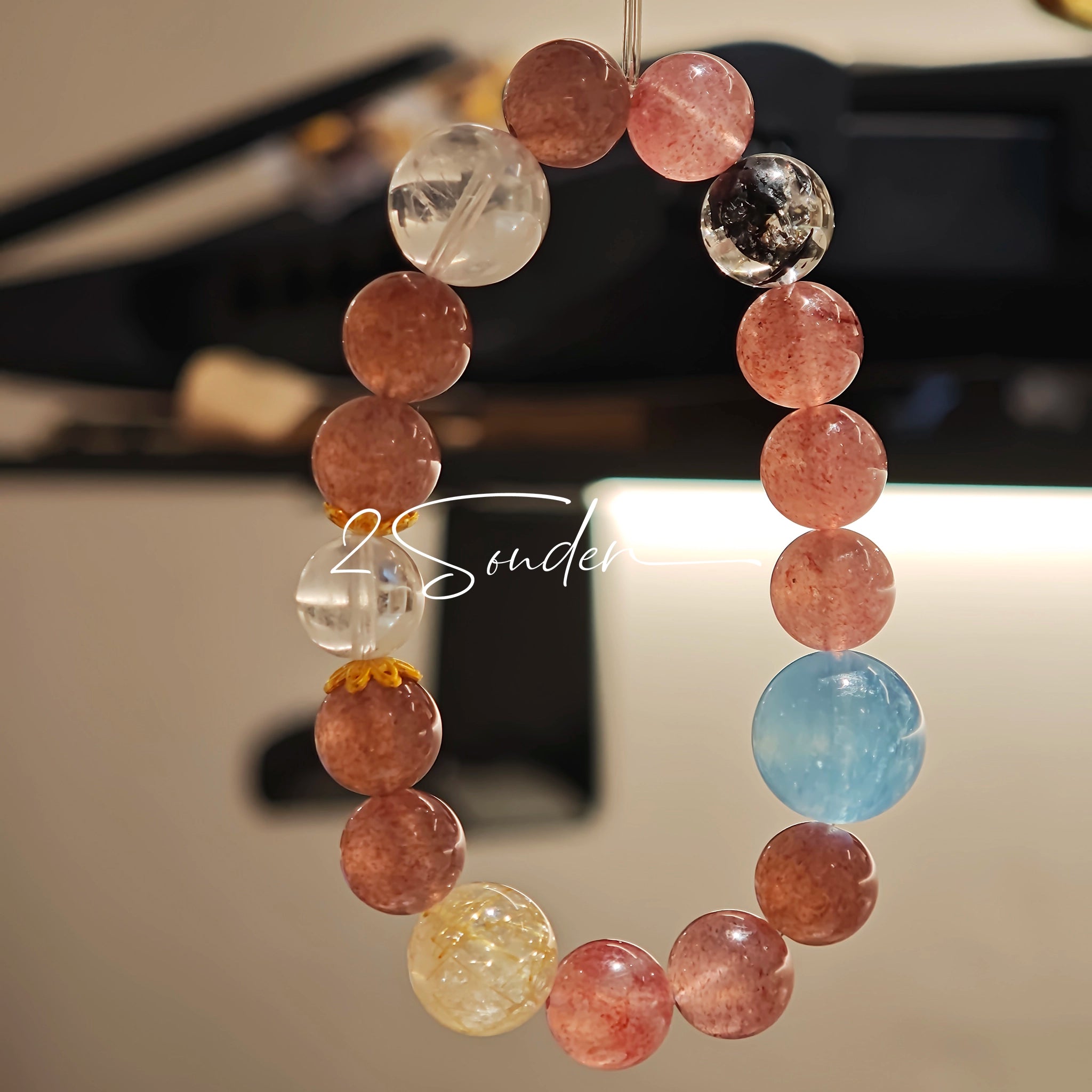 This bracelet is centered around a prominent round light blue aquamarine bead, surrounded by rich reddish-brown strawberry quartz beads. It is accented with clear crystal, black rutilated quartz, and golden rutilated quartz beads, along with delicate gold spacers, creating a harmonious natural stone design.