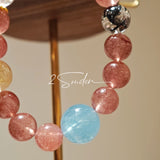 This bracelet is centered around a prominent round light blue aquamarine bead, surrounded by rich reddish-brown strawberry quartz beads. It is accented with clear crystal, black rutilated quartz, and golden rutilated quartz beads, along with delicate gold spacers, creating a harmonious natural stone design.