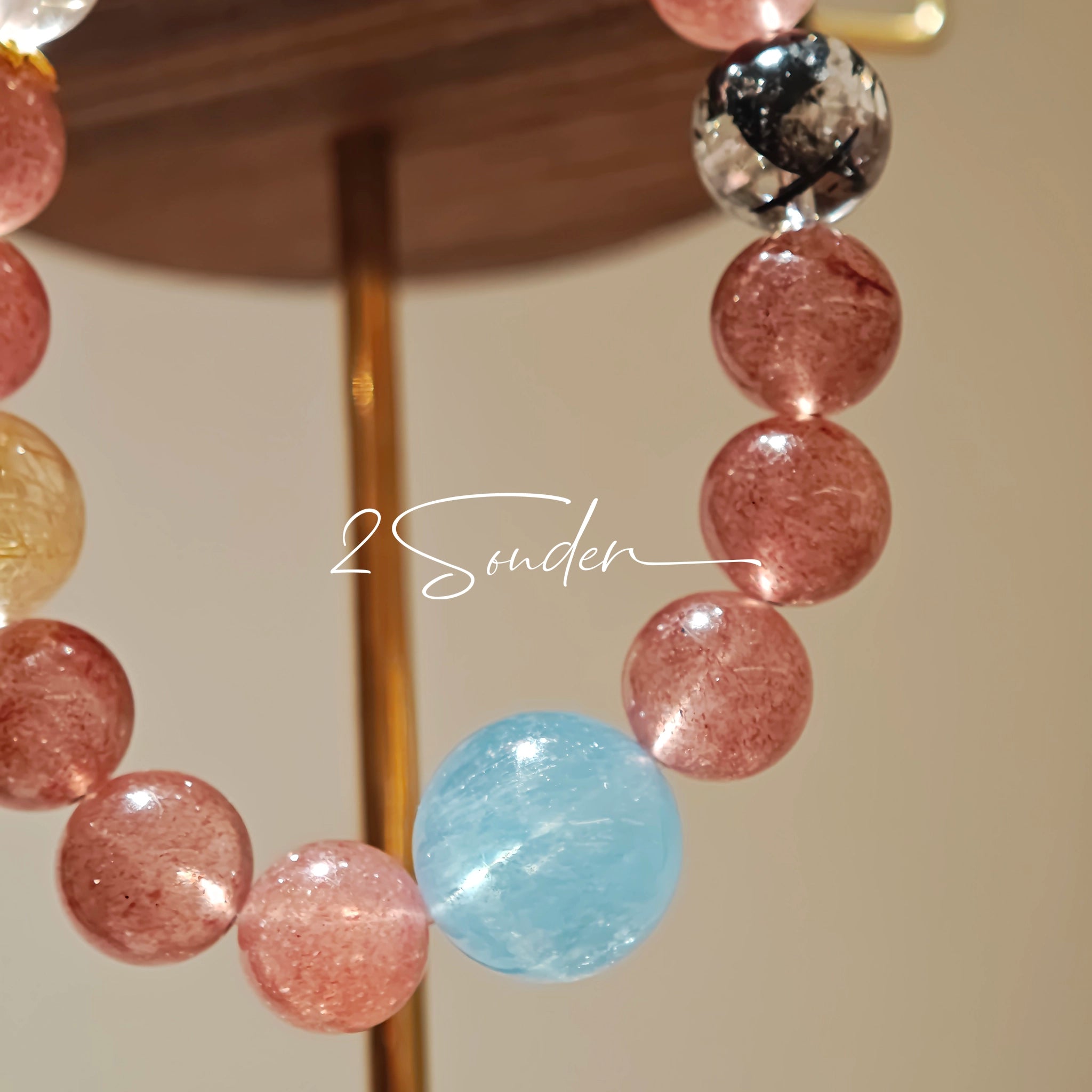 This bracelet is centered around a prominent round light blue aquamarine bead, surrounded by rich reddish-brown strawberry quartz beads. It is accented with clear crystal, black rutilated quartz, and golden rutilated quartz beads, along with delicate gold spacers, creating a harmonious natural stone design.