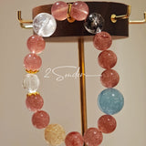 This bracelet is centered around a prominent round light blue aquamarine bead, surrounded by rich reddish-brown strawberry quartz beads. It is accented with clear crystal, black rutilated quartz, and golden rutilated quartz beads, along with delicate gold spacers, creating a harmonious natural stone design.