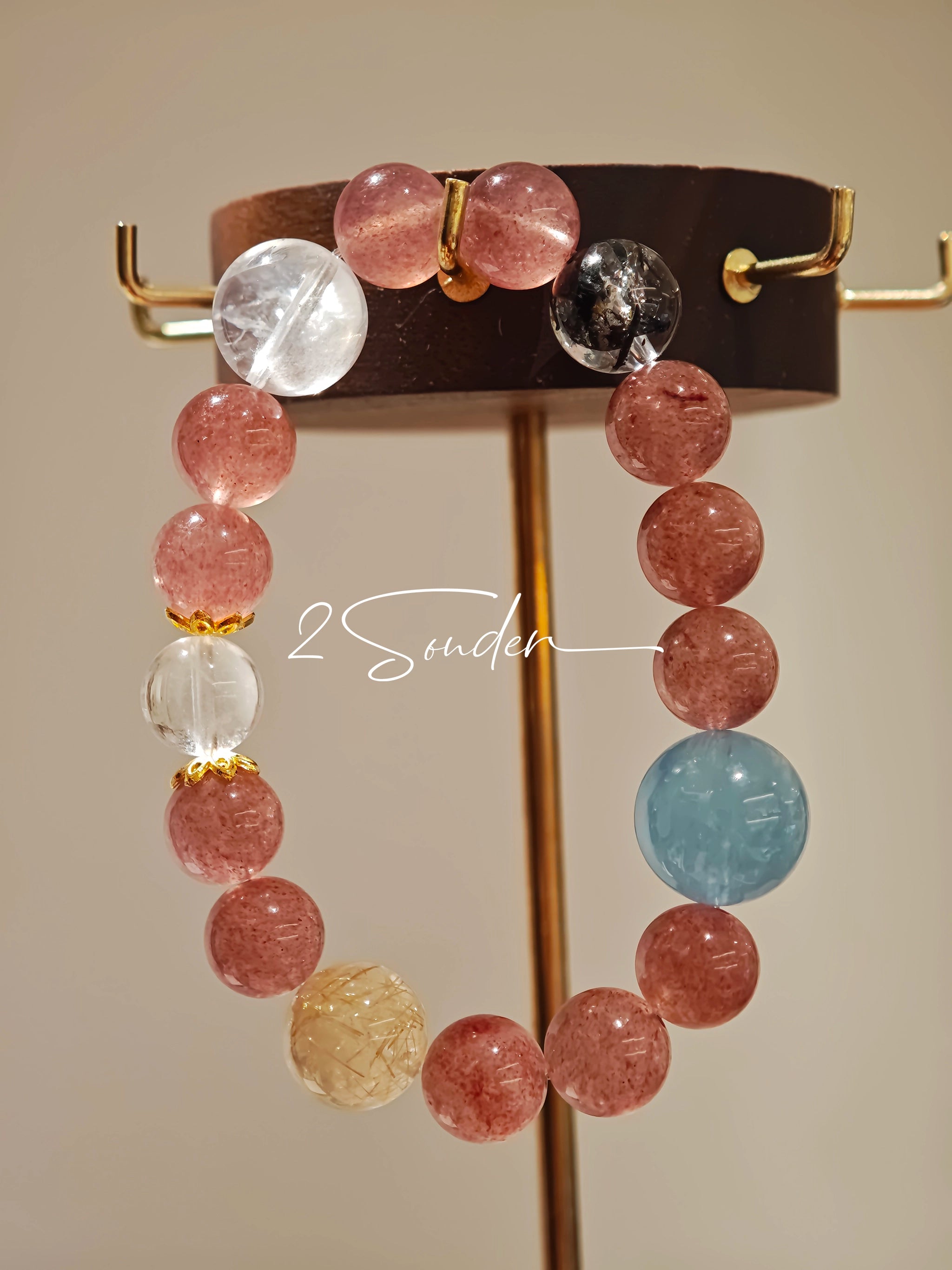 This bracelet is centered around a prominent round light blue aquamarine bead, surrounded by rich reddish-brown strawberry quartz beads. It is accented with clear crystal, black rutilated quartz, and golden rutilated quartz beads, along with delicate gold spacers, creating a harmonious natural stone design.