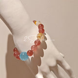 This bracelet is centered around a prominent round light blue aquamarine bead, surrounded by rich reddish-brown strawberry quartz beads. It is accented with clear crystal, black rutilated quartz, and golden rutilated quartz beads, along with delicate gold spacers, creating a harmonious natural stone design.