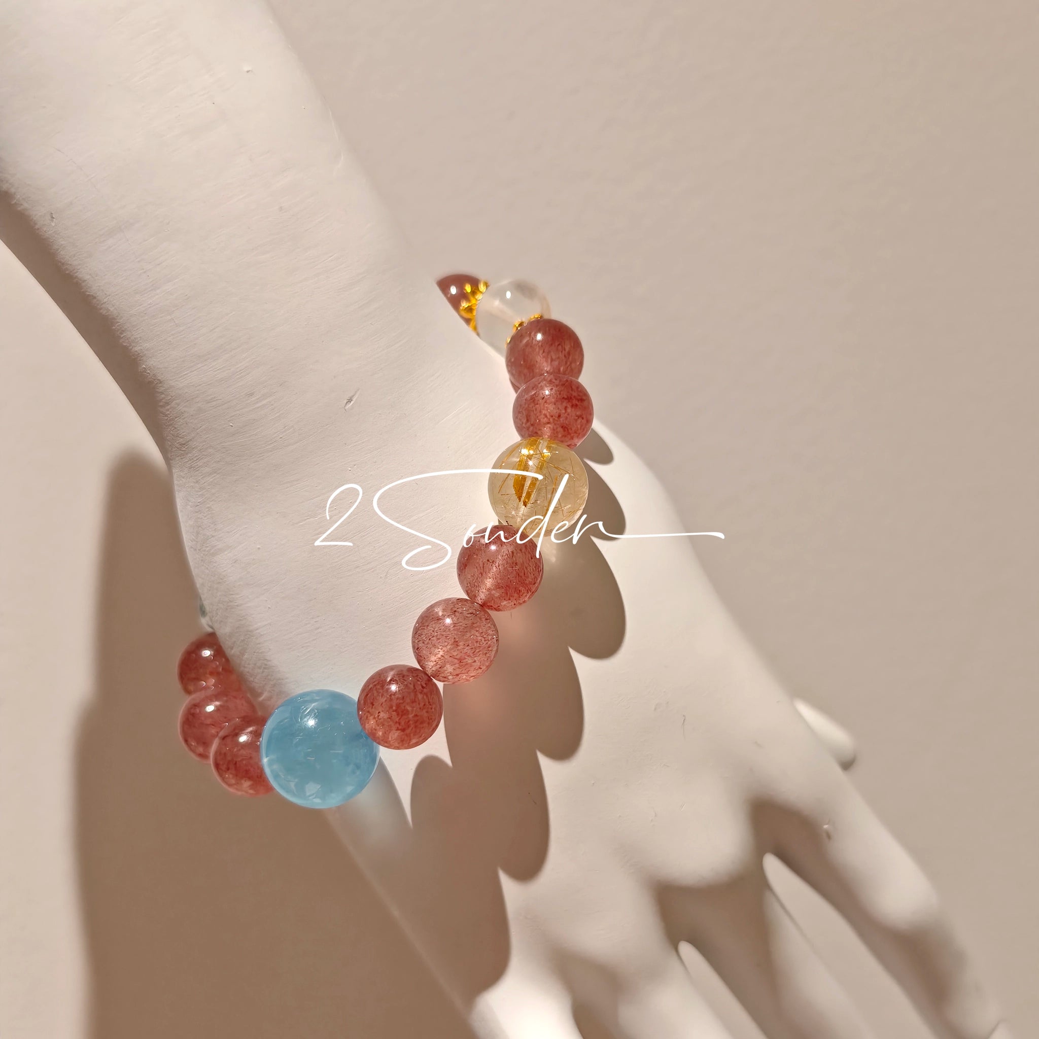 This bracelet is centered around a prominent round light blue aquamarine bead, surrounded by rich reddish-brown strawberry quartz beads. It is accented with clear crystal, black rutilated quartz, and golden rutilated quartz beads, along with delicate gold spacers, creating a harmonious natural stone design.