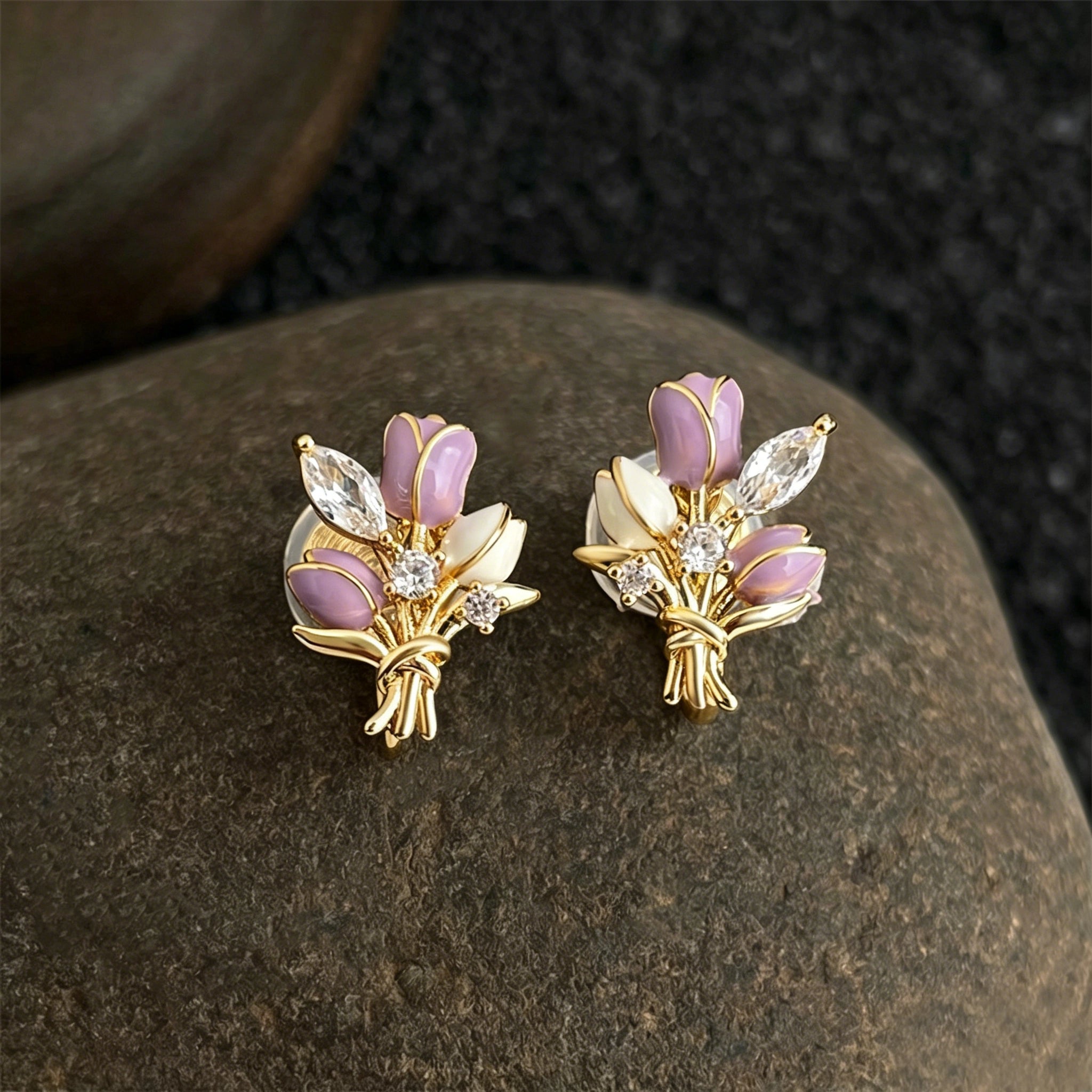 These stud earrings feature an elegant bouquet design, crafted with a thick 18K real gold plating. The arrangement showcases delicate purple and white enamel tulip flowers, accented with sparkling marquise and round-cut cubic zirconia stones, all set in a polished gold-tone metal structure tied with a decorative knot at the base. The overall style is romantic and refined, perfect for adding a touch of floral charm to any look.