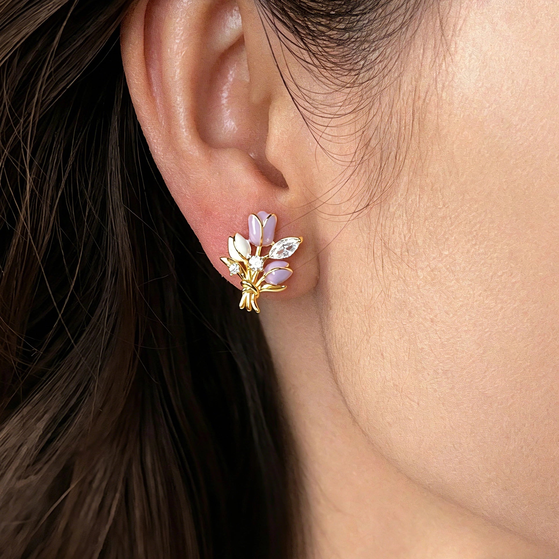 These stud earrings feature an elegant bouquet design, crafted with a thick 18K real gold plating. The arrangement showcases delicate purple and white enamel tulip flowers, accented with sparkling marquise and round-cut cubic zirconia stones, all set in a polished gold-tone metal structure tied with a decorative knot at the base. The overall style is romantic and refined, perfect for adding a touch of floral charm to any look.
