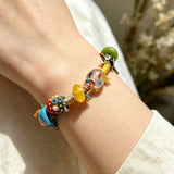 This handmade boho bracelet bursts with vibrant dopamine colors, featuring hand-painted clay beads, twisted linen threads, and quirky sculpted charms. Every bead and wrapped fiber is carefully crafted, bringing playful, retro artistic vibes to your wrist. It is a unique wearable art piece full of whimsical details.