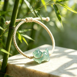 This vintage hand-woven bracelet features a lovely translucent jade-green kitten charm, paired with soft off-white braided cord. The fresh natural bamboo backdrop highlights its gentle, playful dopamine style, perfect as a delicate daily accessory. It has an adjustable knotted design for a comfortable fit on different wrist sizes.