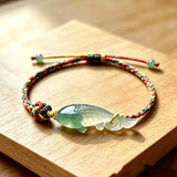This hand-woven bracelet features a delicate translucent jade fish charm, symbolizing good fortune and abundance. Its vibrant multi-colored braided cord blends retro aesthetics with playful dopamine styling, finished with adjustable knots for a comfortable fit.