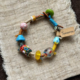 This handmade boho bracelet bursts with vibrant dopamine colors, featuring hand-painted clay beads, twisted linen threads, and quirky sculpted charms. Every bead and wrapped fiber is carefully crafted, bringing playful, retro artistic vibes to your wrist. It is a unique wearable art piece full of whimsical details.