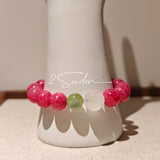 This beaded bracelet is mainly made of round, rosy-pink rhodonite beads with a delicate marbled texture. It is accented by one pale green Xiuyan jade bead (in the "green grape milk cap" style) and one translucent white phantom quartz bead, creating a soft color contrast against the dominant pink hue. The smooth, polished stones give the bracelet a gentle, natural look.