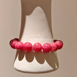 This beaded bracelet is mainly made of round, rosy-pink rhodonite beads with a delicate marbled texture. It is accented by one pale green Xiuyan jade bead (in the "green grape milk cap" style) and one translucent white phantom quartz bead, creating a soft color contrast against the dominant pink hue. The smooth, polished stones give the bracelet a gentle, natural look.