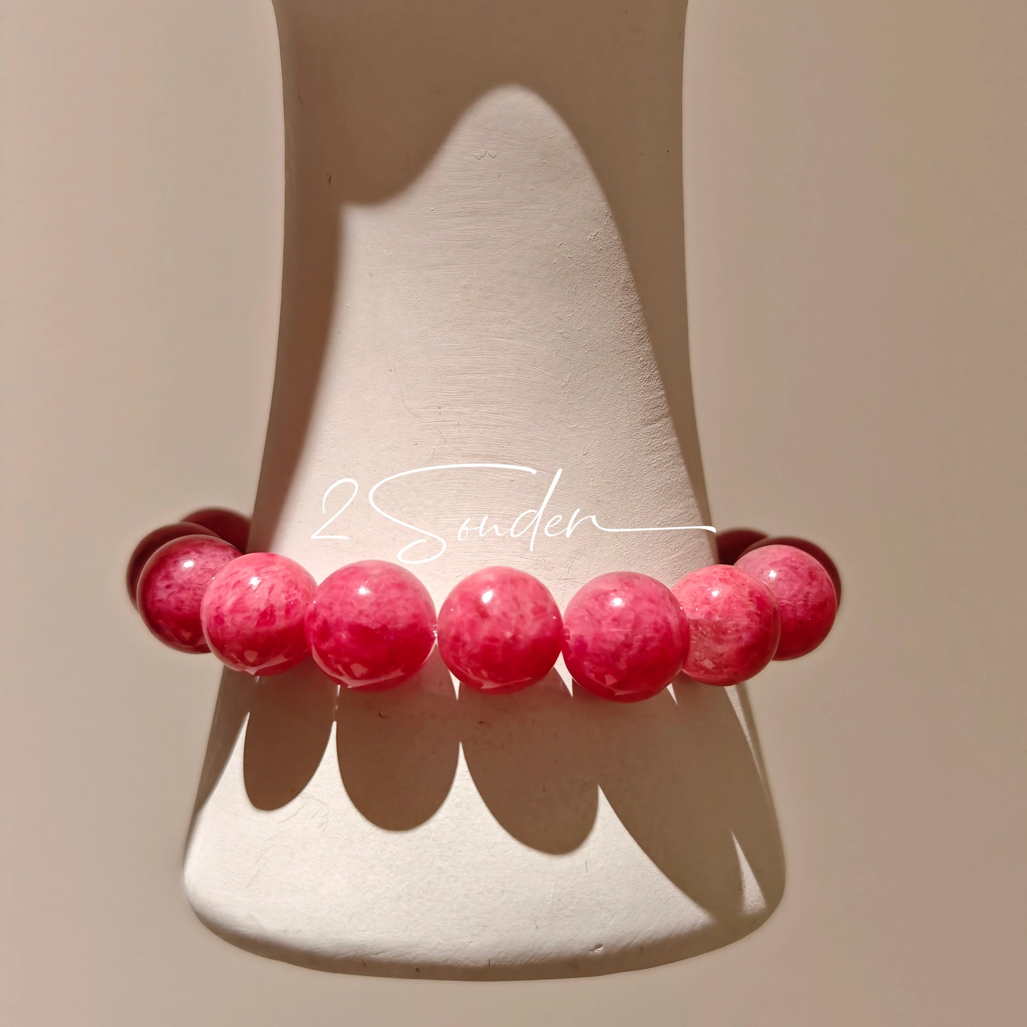 This beaded bracelet is mainly made of round, rosy-pink rhodonite beads with a delicate marbled texture. It is accented by one pale green Xiuyan jade bead (in the "green grape milk cap" style) and one translucent white phantom quartz bead, creating a soft color contrast against the dominant pink hue. The smooth, polished stones give the bracelet a gentle, natural look.