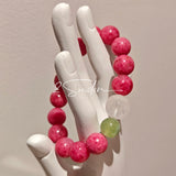 This beaded bracelet is mainly made of round, rosy-pink rhodonite beads with a delicate marbled texture. It is accented by one pale green Xiuyan jade bead (in the "green grape milk cap" style) and one translucent white phantom quartz bead, creating a soft color contrast against the dominant pink hue. The smooth, polished stones give the bracelet a gentle, natural look.