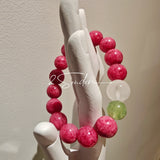 This beaded bracelet is mainly made of round, rosy-pink rhodonite beads with a delicate marbled texture. It is accented by one pale green Xiuyan jade bead (in the "green grape milk cap" style) and one translucent white phantom quartz bead, creating a soft color contrast against the dominant pink hue. The smooth, polished stones give the bracelet a gentle, natural look.