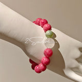 This beaded bracelet is mainly made of round, rosy-pink rhodonite beads with a delicate marbled texture. It is accented by one pale green Xiuyan jade bead (in the "green grape milk cap" style) and one translucent white phantom quartz bead, creating a soft color contrast against the dominant pink hue. The smooth, polished stones give the bracelet a gentle, natural look.