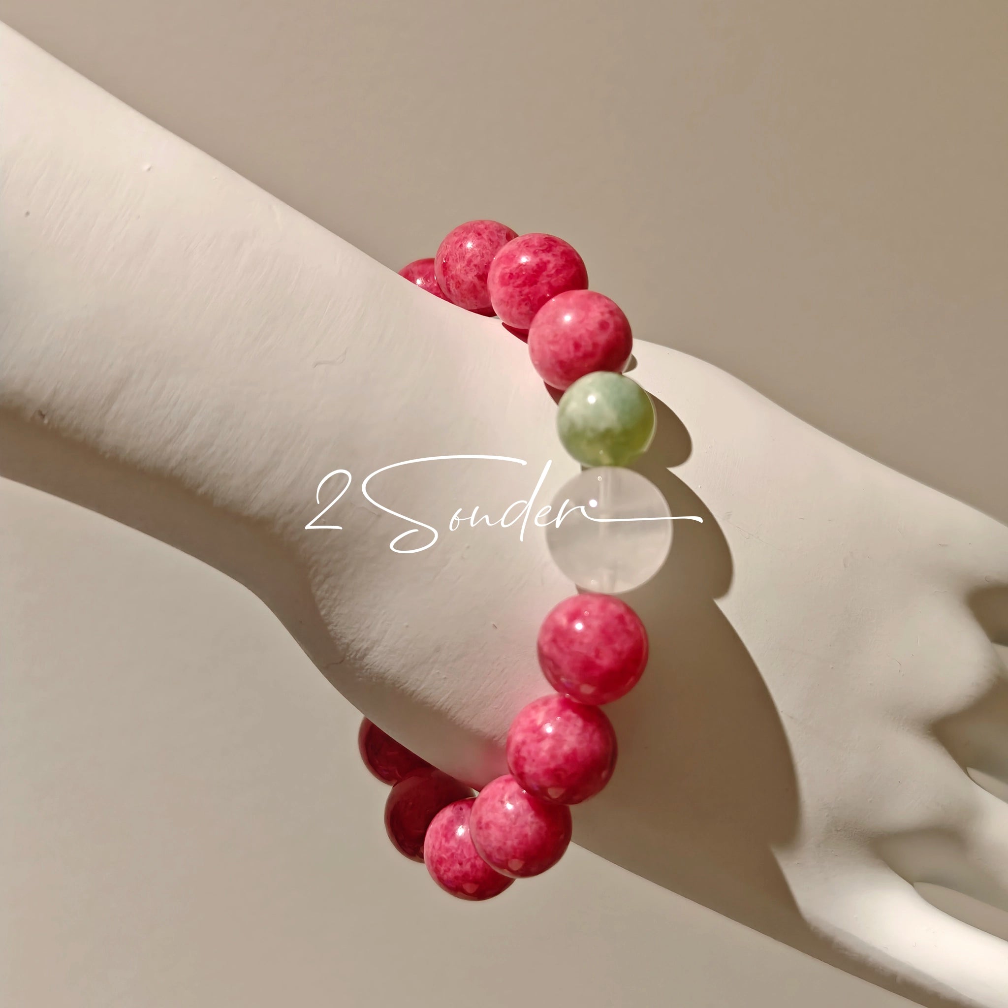 This beaded bracelet is mainly made of round, rosy-pink rhodonite beads with a delicate marbled texture. It is accented by one pale green Xiuyan jade bead (in the "green grape milk cap" style) and one translucent white phantom quartz bead, creating a soft color contrast against the dominant pink hue. The smooth, polished stones give the bracelet a gentle, natural look.