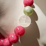 This beaded bracelet is mainly made of round, rosy-pink rhodonite beads with a delicate marbled texture. It is accented by one pale green Xiuyan jade bead (in the "green grape milk cap" style) and one translucent white phantom quartz bead, creating a soft color contrast against the dominant pink hue. The smooth, polished stones give the bracelet a gentle, natural look.