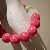 This beaded bracelet is mainly made of round, rosy-pink rhodonite beads with a delicate marbled texture. It is accented by one pale green Xiuyan jade bead (in the "green grape milk cap" style) and one translucent white phantom quartz bead, creating a soft color contrast against the dominant pink hue. The smooth, polished stones give the bracelet a gentle, natural look.
