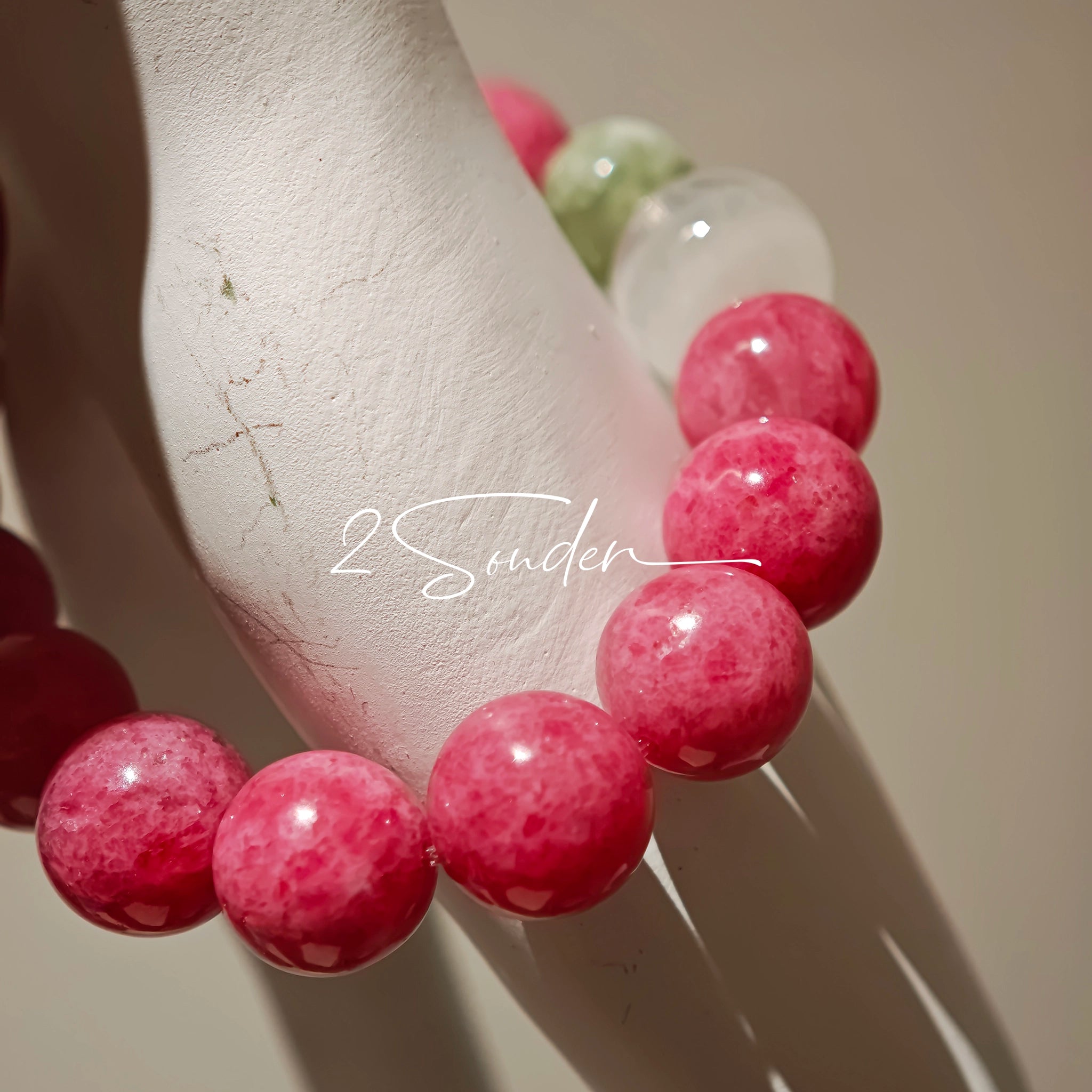 This beaded bracelet is mainly made of round, rosy-pink rhodonite beads with a delicate marbled texture. It is accented by one pale green Xiuyan jade bead (in the "green grape milk cap" style) and one translucent white phantom quartz bead, creating a soft color contrast against the dominant pink hue. The smooth, polished stones give the bracelet a gentle, natural look.