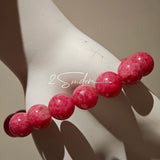 This beaded bracelet is mainly made of round, rosy-pink rhodonite beads with a delicate marbled texture. It is accented by one pale green Xiuyan jade bead (in the "green grape milk cap" style) and one translucent white phantom quartz bead, creating a soft color contrast against the dominant pink hue. The smooth, polished stones give the bracelet a gentle, natural look.