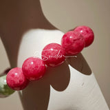 This beaded bracelet is mainly made of round, rosy-pink rhodonite beads with a delicate marbled texture. It is accented by one pale green Xiuyan jade bead (in the "green grape milk cap" style) and one translucent white phantom quartz bead, creating a soft color contrast against the dominant pink hue. The smooth, polished stones give the bracelet a gentle, natural look.