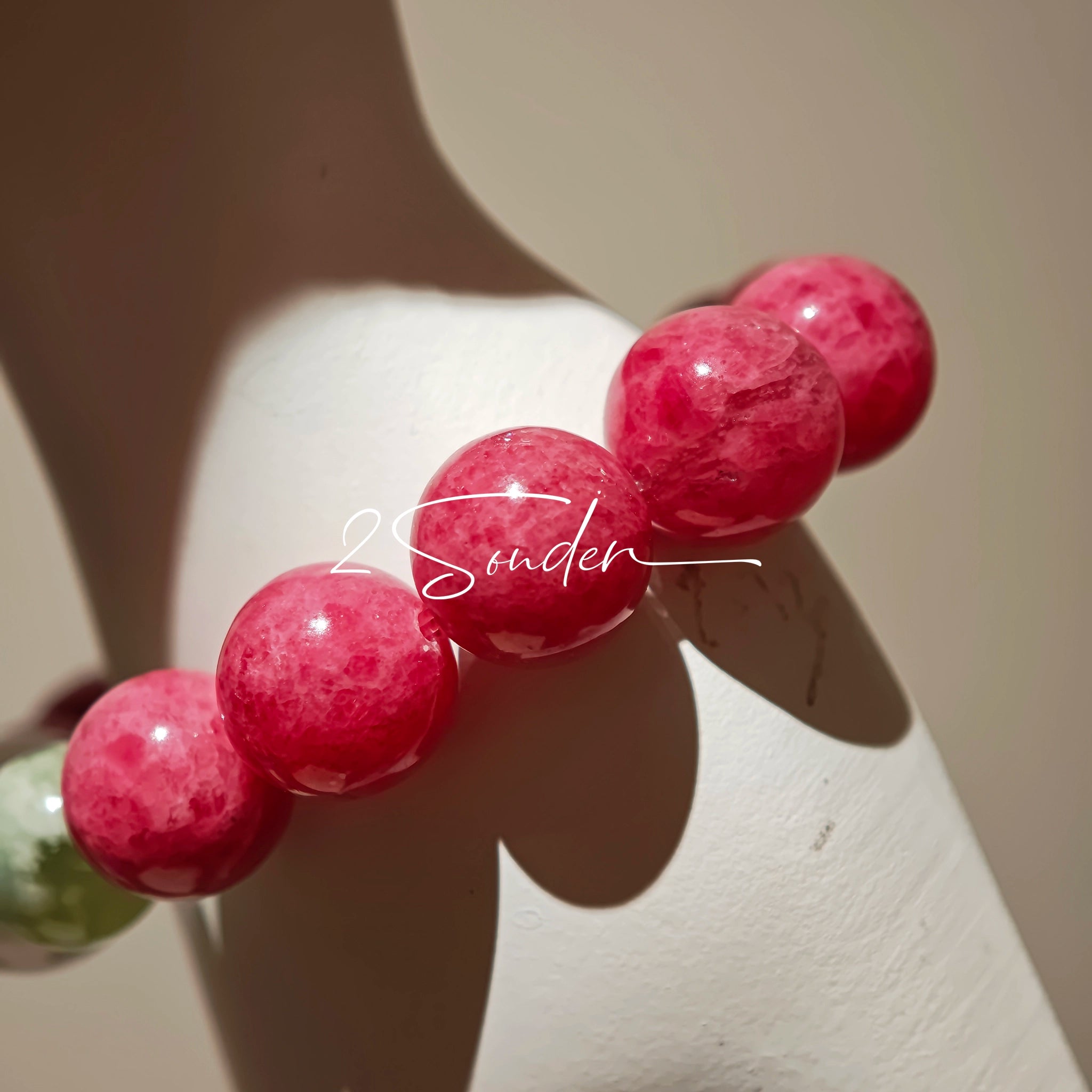 This beaded bracelet is mainly made of round, rosy-pink rhodonite beads with a delicate marbled texture. It is accented by one pale green Xiuyan jade bead (in the "green grape milk cap" style) and one translucent white phantom quartz bead, creating a soft color contrast against the dominant pink hue. The smooth, polished stones give the bracelet a gentle, natural look.