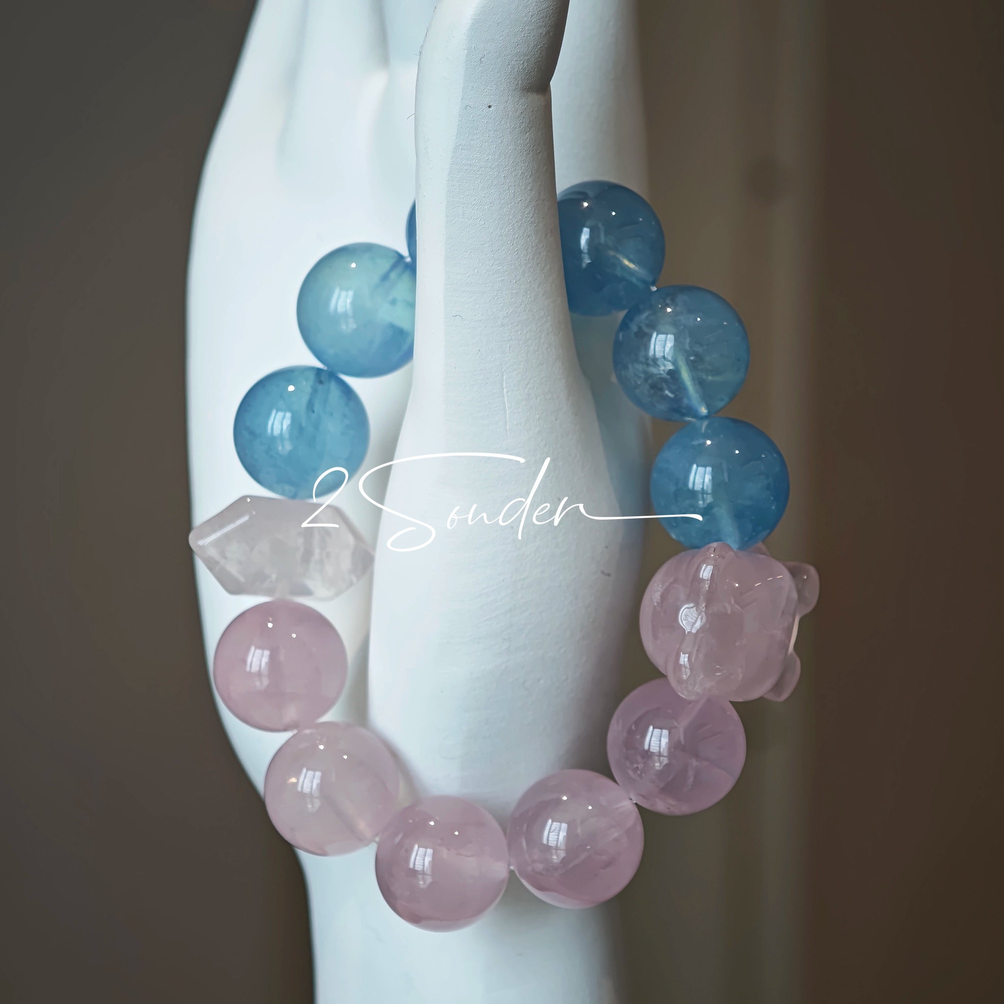 This bracelet consists of rose quartz and aquamarine. The bracelet features a bead pendant and a rhombic spacer, both of which are made of rose quartz. The bracelet is a combination of pink and blue colors.