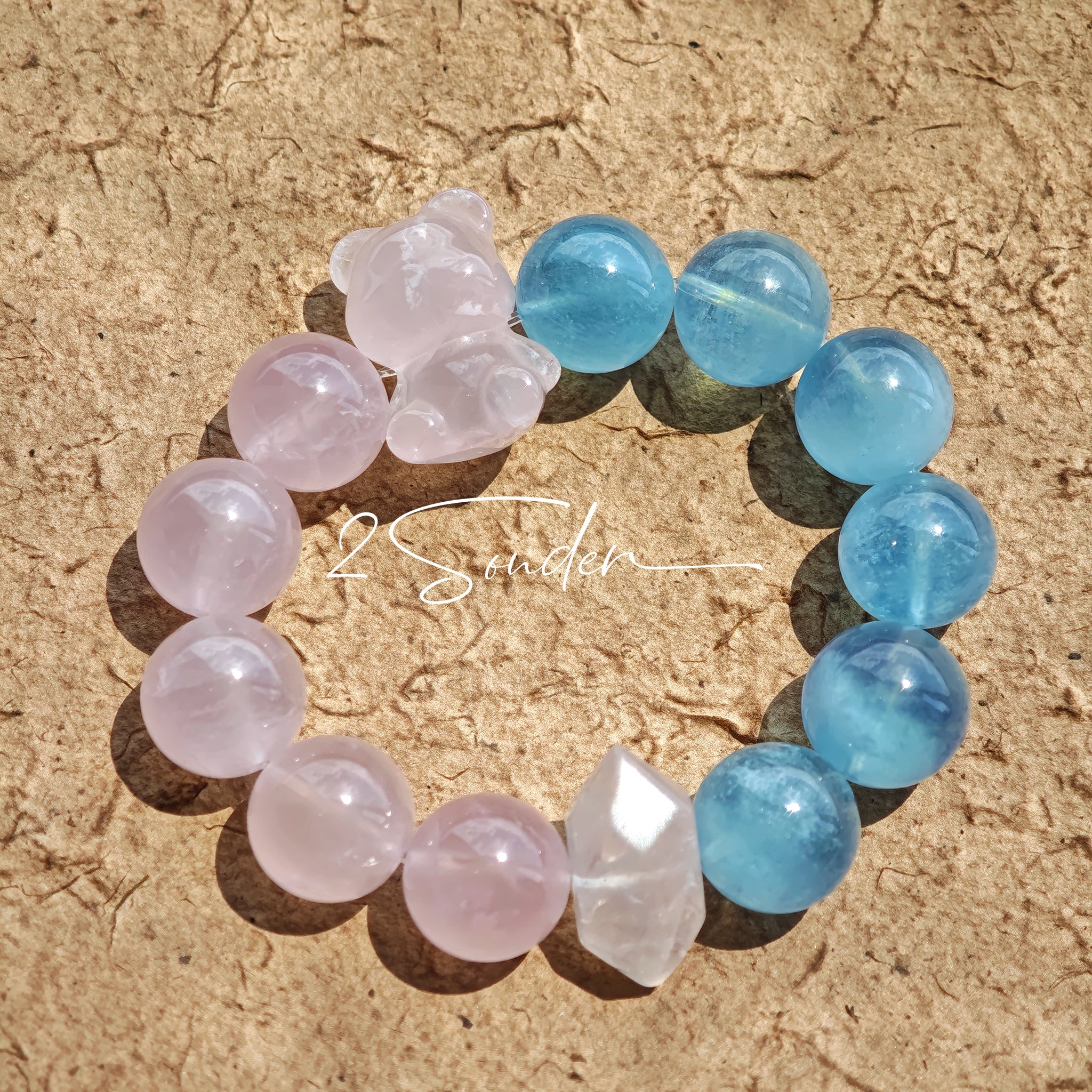 This bracelet consists of rose quartz and aquamarine. The bracelet features a bead pendant and a rhombic spacer, both of which are made of rose quartz. The bracelet is a combination of pink and blue colors.