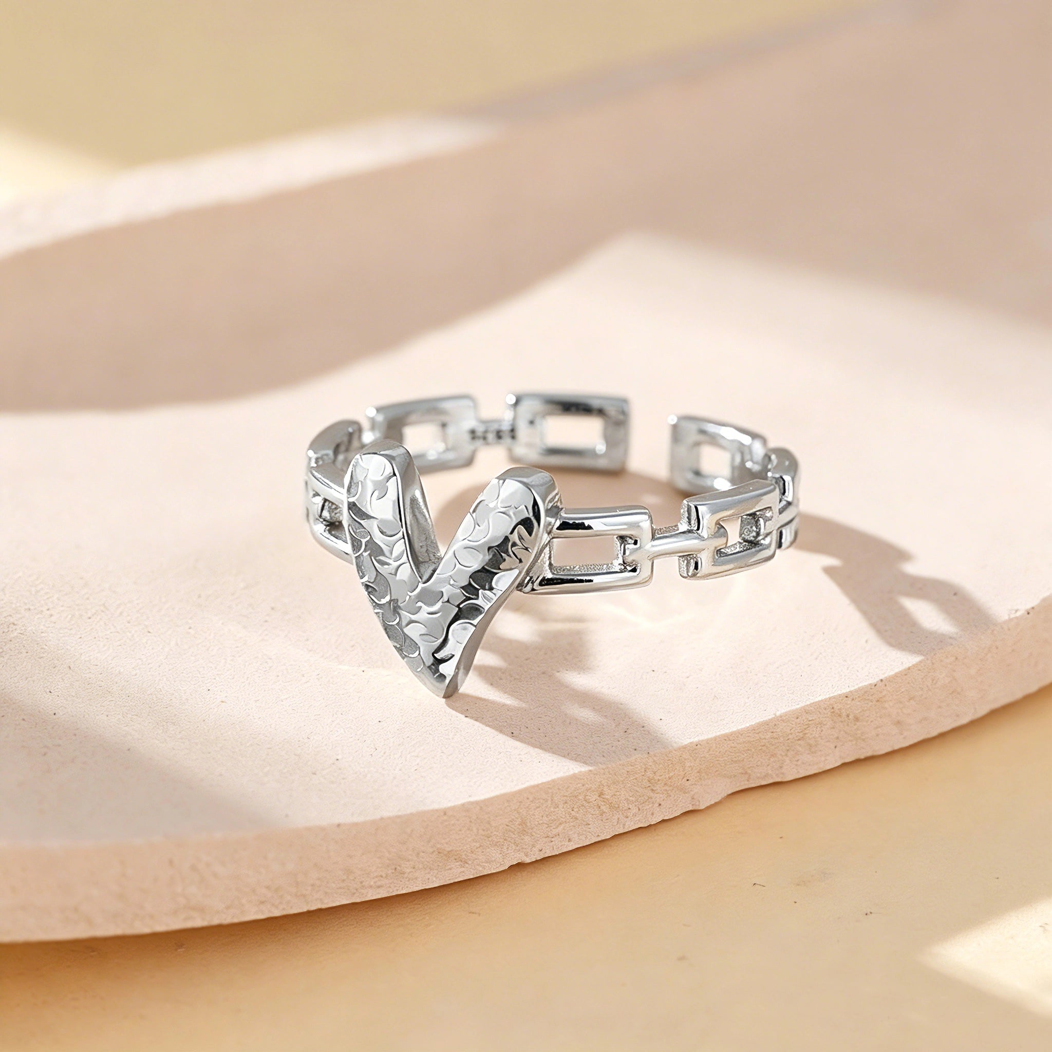 This is an adjustable open ring crafted from S925 sterling silver. It features a modern chain-link band paired with a textured heart-shaped centerpiece, boasting a "crushed ice" finish that delivers a sparkling, dimensional look. The polished silver tone lends a sleek, contemporary vibe to this versatile piece.