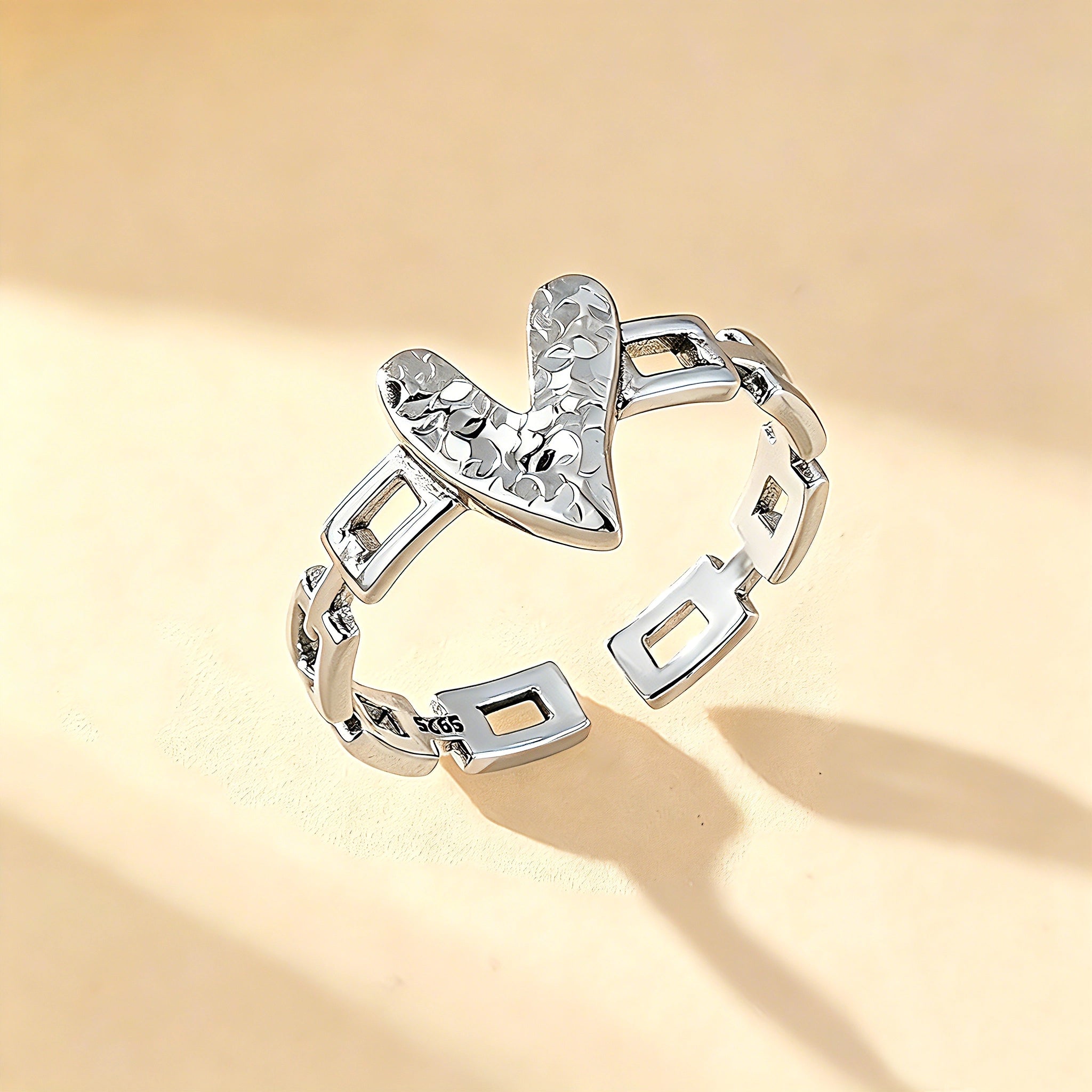 This is an adjustable open ring crafted from S925 sterling silver. It features a modern chain-link band paired with a textured heart-shaped centerpiece, boasting a "crushed ice" finish that delivers a sparkling, dimensional look. The polished silver tone lends a sleek, contemporary vibe to this versatile piece.