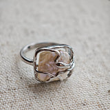This adjustable S925 sterling silver ring features a striking baroque pearl at its center, set within an organic, flowing silver frame that wraps around the irregular, lustrous gemstone. The open, sculptural metalwork creates a modern, artistic silhouette, showcasing the pearl's natural, one-of-a-kind texture and soft iridescence. The sleek, polished silver band complements the unique pearl, making it a standout piece with a contemporary, bohemian aesthetic.