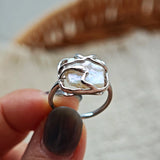 This adjustable S925 sterling silver ring features a striking baroque pearl at its center, set within an organic, flowing silver frame that wraps around the irregular, lustrous gemstone. The open, sculptural metalwork creates a modern, artistic silhouette, showcasing the pearl's natural, one-of-a-kind texture and soft iridescence. The sleek, polished silver band complements the unique pearl, making it a standout piece with a contemporary, bohemian aesthetic.