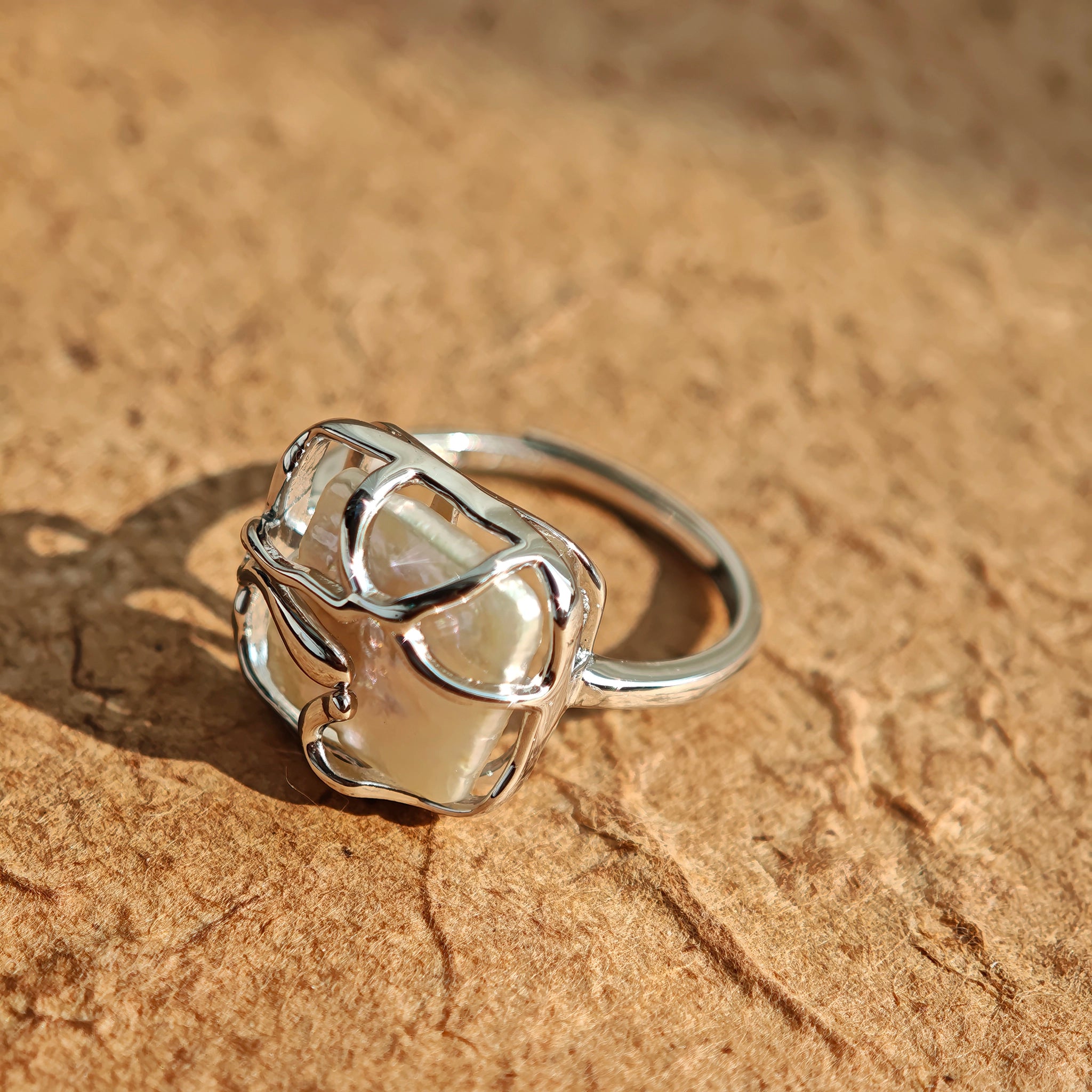 This adjustable S925 sterling silver ring features a striking baroque pearl at its center, set within an organic, flowing silver frame that wraps around the irregular, lustrous gemstone. The open, sculptural metalwork creates a modern, artistic silhouette, showcasing the pearl's natural, one-of-a-kind texture and soft iridescence. The sleek, polished silver band complements the unique pearl, making it a standout piece with a contemporary, bohemian aesthetic.