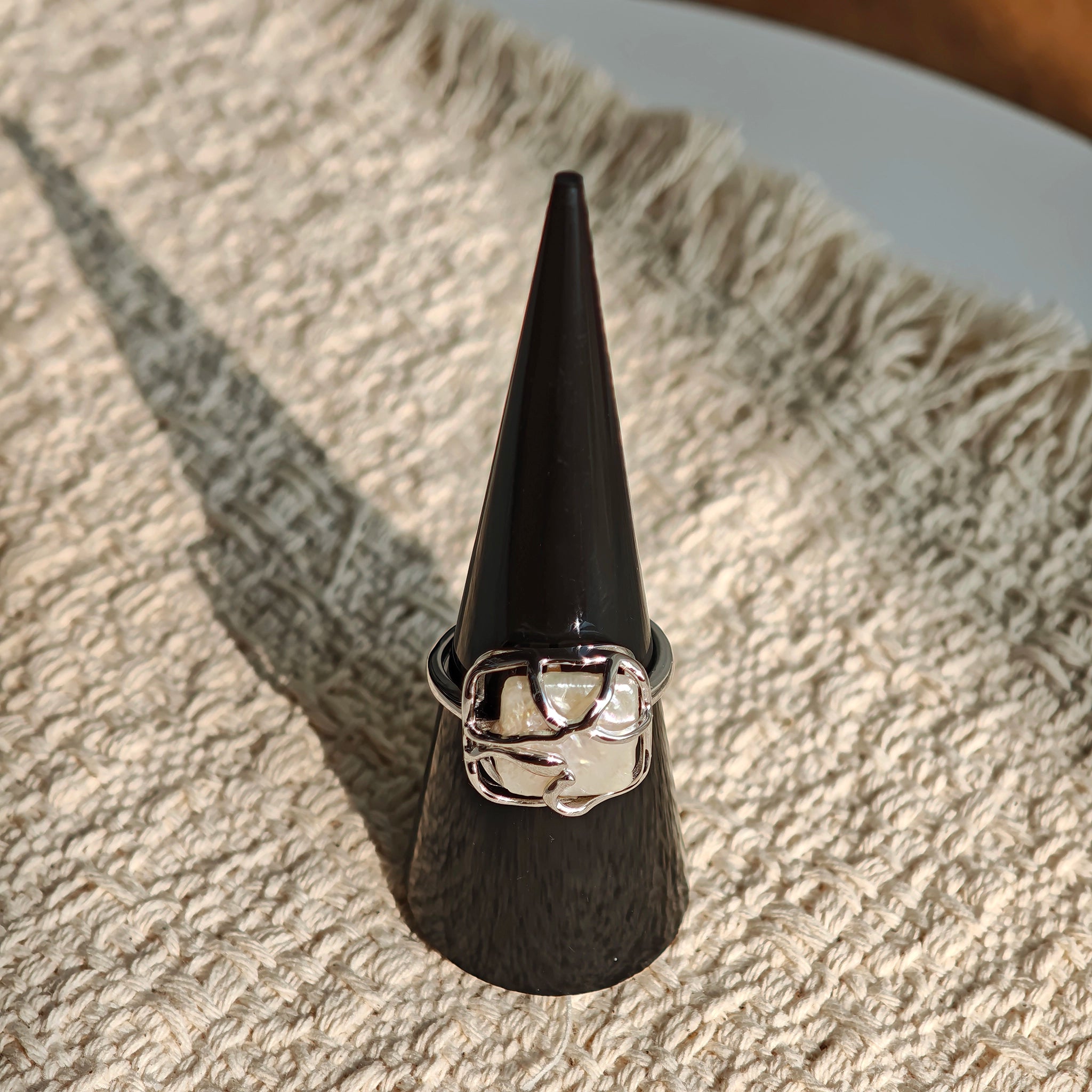 This adjustable S925 sterling silver ring features a striking baroque pearl at its center, set within an organic, flowing silver frame that wraps around the irregular, lustrous gemstone. The open, sculptural metalwork creates a modern, artistic silhouette, showcasing the pearl's natural, one-of-a-kind texture and soft iridescence. The sleek, polished silver band complements the unique pearl, making it a standout piece with a contemporary, bohemian aesthetic.
