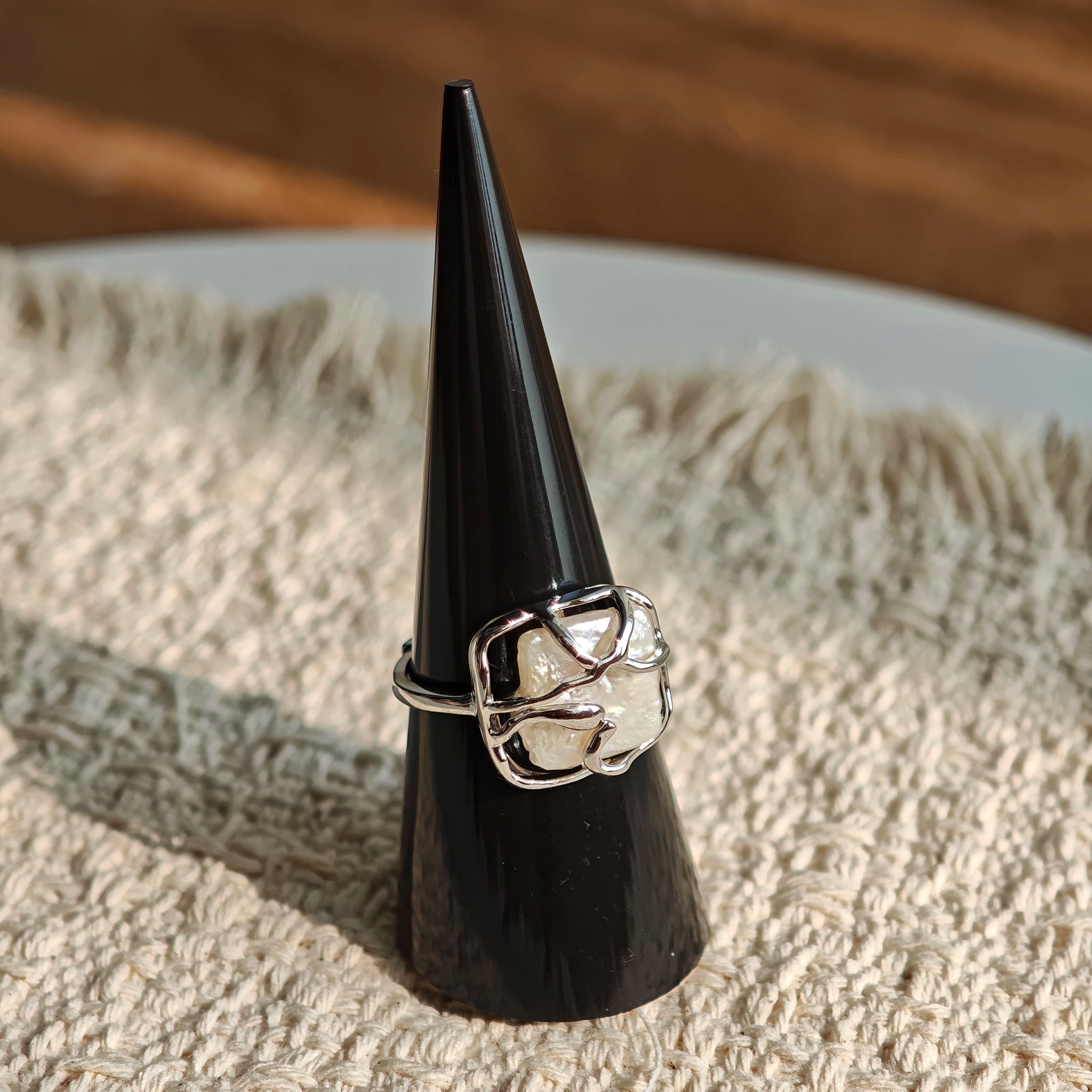 This adjustable S925 sterling silver ring features a striking baroque pearl at its center, set within an organic, flowing silver frame that wraps around the irregular, lustrous gemstone. The open, sculptural metalwork creates a modern, artistic silhouette, showcasing the pearl's natural, one-of-a-kind texture and soft iridescence. The sleek, polished silver band complements the unique pearl, making it a standout piece with a contemporary, bohemian aesthetic.