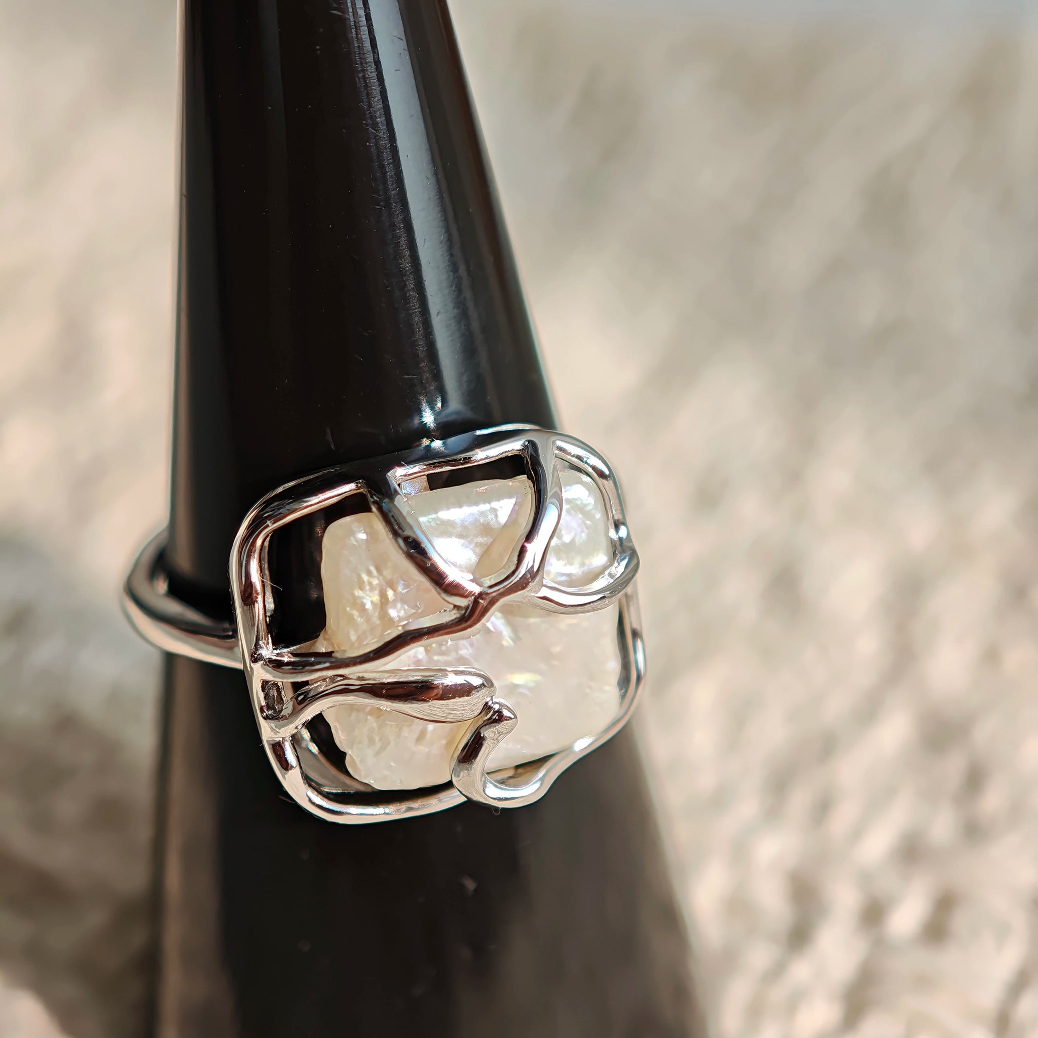 This adjustable S925 sterling silver ring features a striking baroque pearl at its center, set within an organic, flowing silver frame that wraps around the irregular, lustrous gemstone. The open, sculptural metalwork creates a modern, artistic silhouette, showcasing the pearl's natural, one-of-a-kind texture and soft iridescence. The sleek, polished silver band complements the unique pearl, making it a standout piece with a contemporary, bohemian aesthetic.